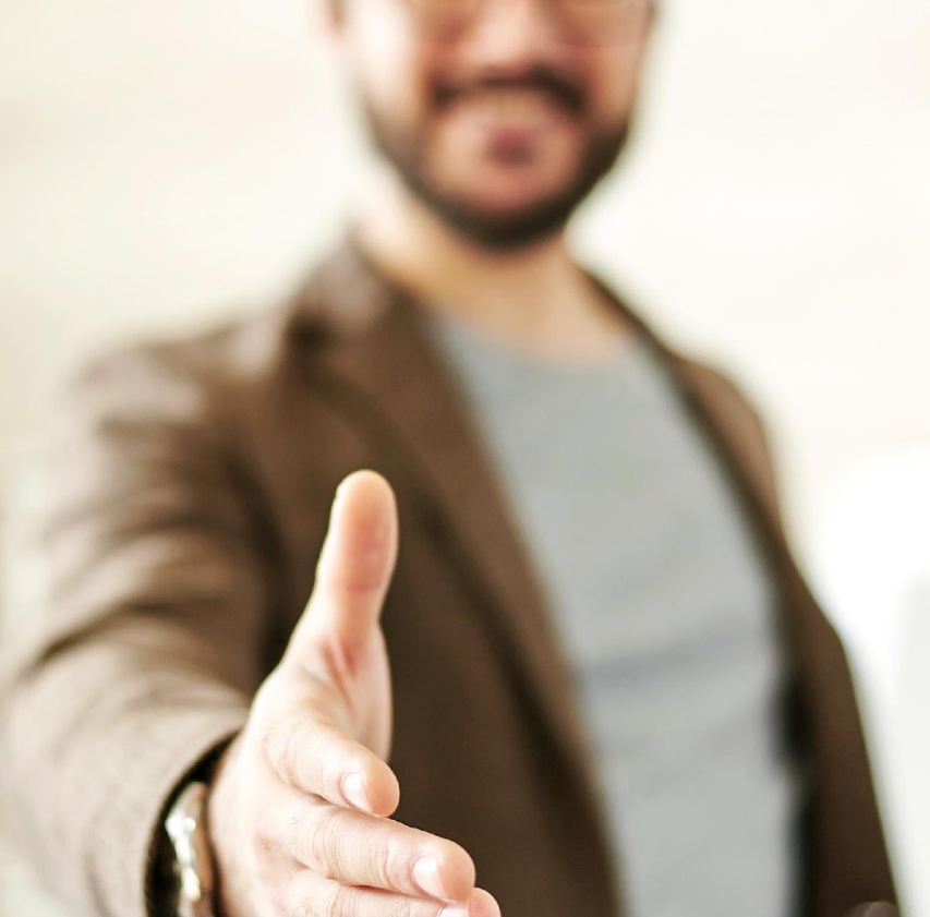 Person extending hand for a handshake wearing a brown sport coat