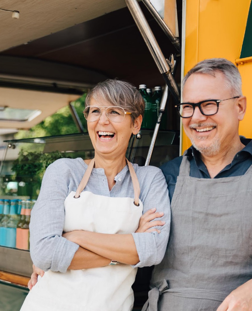 Two people wearing aprons in front of food truck smiling